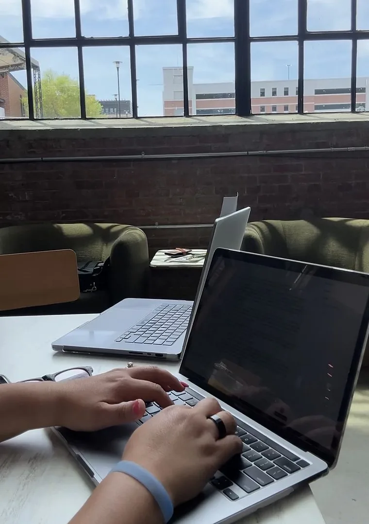 Sheri typing on her laptop at a table by a big warehouse window